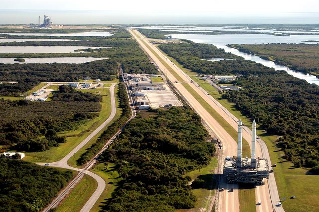 NASA image: KENNEDY SPACE CENTER, FLA. -  The crawler transporter slowly moves the Mobile Launcher Platform (MLP), carrying a set of twin solid rocket boosters, away from the Vehicle Assembly Building (VAB) in support of engineering analysis vibration tests on the crawler and MLP.   In the distance, at left, is Launch Pad 39A.  The water on the right of the crawlerway is the Banana River.  The crawler is moving at various speeds up to 1 mph in an effort to achieve vibration data gathering goals as it leaves the VAB and then returns.  The boosters are braced at the top for stability.  The primary purpose of these rollout tests is to gather data to develop future maintenance requirements on the transport equipment and the flight hardware. Various parts of the MLP and crawler transporter have been instrumented with vibration data collection equipment.