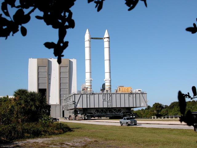 NASA image: KENNEDY SPACE CENTER, FLA. -  The crawler transporter slowly moves the Mobile Launcher Platform (MLP), carrying a set of twin solid rocket boosters, away from the Vehicle Assembly Building (VAB) in support of engineering analysis vibration tests on the crawler and MLP.   The crawler is moving at various speeds up to 1 mph in an effort to achieve vibration data gathering goals as it leaves the VAB and then returns.  The boosters are braced at the top for stability.  The primary purpose of these rollout tests is to gather data to develop future maintenance requirements on the transport equipment and the flight hardware. Various parts of the MLP and crawler transporter have been instrumented with vibration data collection equipment.