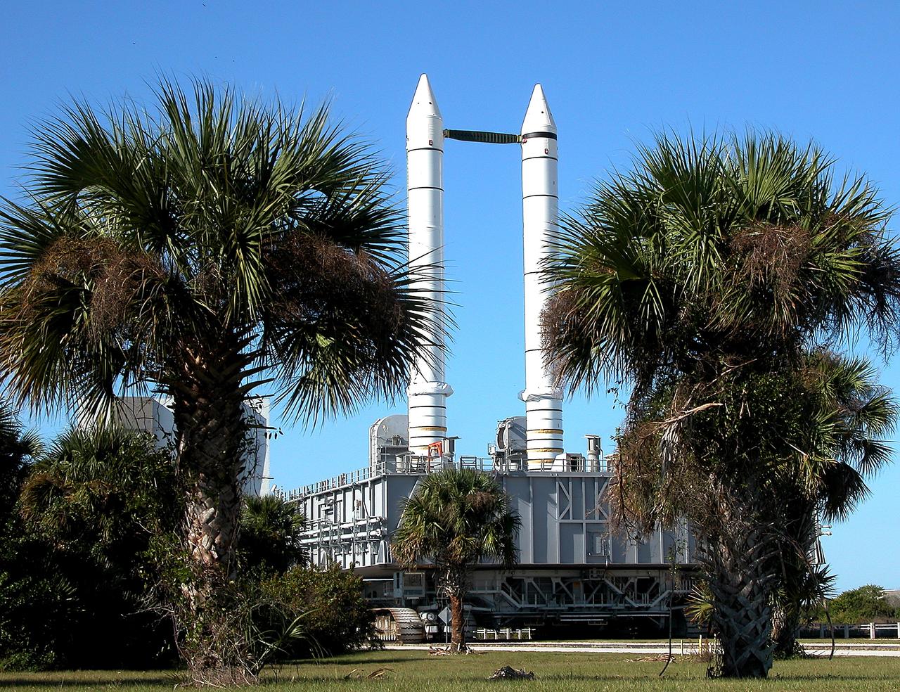KENNEDY SPACE CENTER, FLA. -  Framed between palm trees, solid rocket boosters loom above the Mobile Launcher Platform (MLP) as the crawler transporter slowly moves it along the crawlerway.  The journey is in support of engineering analysis vibration tests on the crawler and MLP.  The crawler is moving at various speeds up to 1 mph in an effort to achieve vibration data gathering goals as it leaves the VAB and then returns.  The boosters are braced at the top for stability. The primary purpose of these rollout tests is to gather data to develop future maintenance requirements on the transport equipment and the flight hardware. Various parts of the MLP and crawler transporter have been instrumented with vibration data collection equipment.