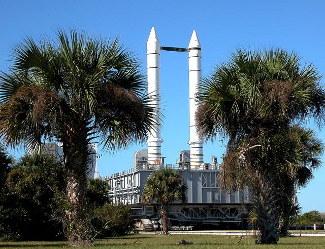 NASA image: KENNEDY SPACE CENTER, FLA. -  Framed between palm trees, solid rocket boosters loom above the Mobile Launcher Platform (MLP) as the crawler transporter slowly moves it along the crawlerway.  The journey is in support of engineering analysis vibration tests on the crawler and MLP.  The crawler is moving at various speeds up to 1 mph in an effort to achieve vibration data gathering goals as it leaves the VAB and then returns.  The boosters are braced at the top for stability. The primary purpose of these rollout tests is to gather data to develop future maintenance requirements on the transport equipment and the flight hardware. Various parts of the MLP and crawler transporter have been instrumented with vibration data collection equipment.