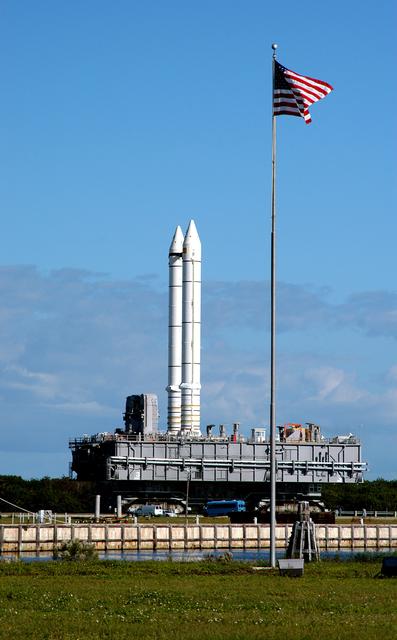NASA image: KENNEDY SPACE CENTER, FLA. - Carrying a set of twin solid rocket boosters, the crawler transporter slowly moves the Mobile Launcher Platform (MLP) past the NASA-KSC News Center where the U.S. flag flies daily.  The journey is in support of engineering analysis vibration tests on the crawler and MLP. The crawler is moving at various speeds up to 1 mph in an effort to achieve vibration data gathering goals as it leaves the VAB and then returns.  The boosters are braced at the top for stability.  The primary purpose of these rollout tests is to gather data to develop future maintenance requirements on the transport equipment and the flight hardware. Various parts of the MLP and crawler transporter have been instrumented with vibration data collection equipment.