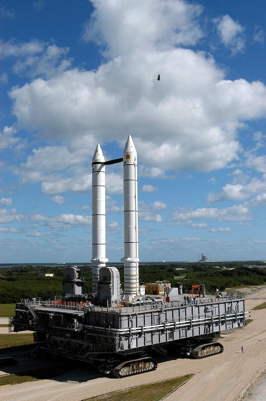 KENNEDY SPACE CENTER, FLA. -  A high-flying bird takes a closer look at the Mobile Launcher Platform (MLP) number 3 with twin solid rocket boosters bolted to it as it crawls toward Launch Pad 39A, in the background.  The crawler is moving along the crawlerway at various speeds up to 1 mph in an effort to achieve vibration data gathering goals as it travels toward Launch Pad 39A and then returns.  The boosters are braced at the top for stability.  The primary purpose of these rollout tests is to gather data to develop future maintenance requirements on the transport equipment and the flight hardware. Various parts of the MLP and crawler transporter have been instrumented with vibration data collection equipment.