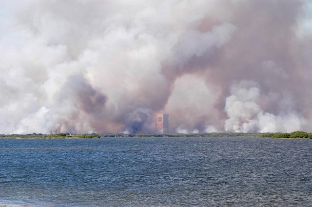 NASA image: KENNEDY SPACE CENTER, FLA. - Smoke from a successful controlled burn near KSC’s Launch Complex 39 surrounds the Vehicle Assembly Building and spreads across the horizon.  The water in the foreground is the Banana River.
