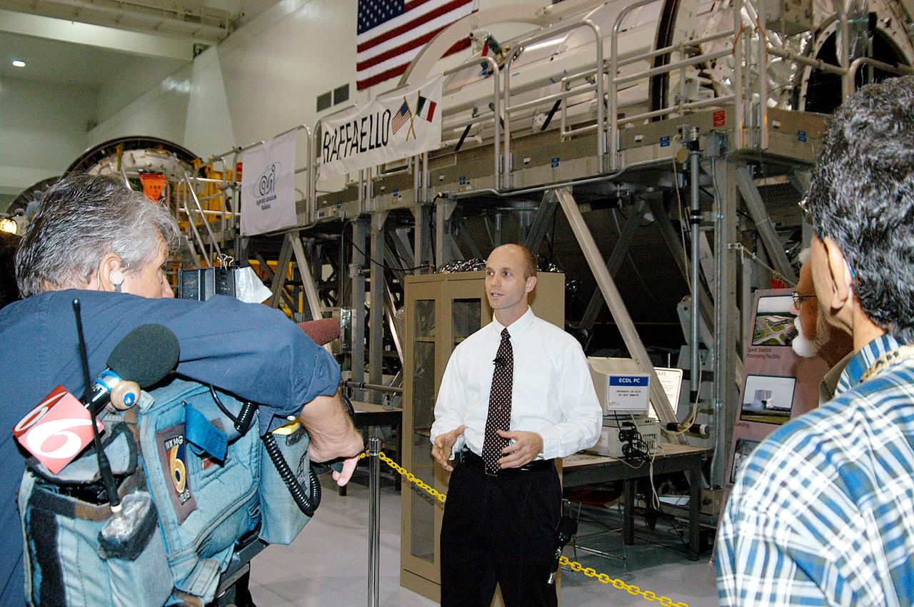 In the Space Station Processing Facility (SSPF), Jim Pope (background), Logistics Flight 1 (LF1) mission manager, International Space Station and Payload Processing, discusses the Multi-Purpose Logistics Modules (MPLMs) with members of the media. MPLMs are pressurized modules that serve as the International Space Station's "moving vans," carrying laboratory racks filled with equipment, experiments and supplies to and from the Station aboard the Space Shuttle. Reporters were invited to commemorate the fifth anniversary of the launch of the first element of the Station with a tour of the facility and had the opportunity to see Space Station hardware that is being processed for deployment once the Space Shuttles return to flight. NASA and Boeing mission managers were on hand to talk about the various hardware elements currently being processed for flight.