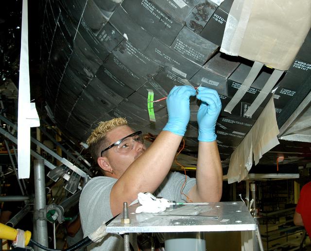 NASA image: KENNEDY SPACE CENTER, FLA. -  In the Orbiter Processing Facility, KSC employee Chris Moore repairs tile on the forward area of the orbiter Discovery. The vehicle has undergone Orbiter Major Modifications in the past year, which includes tile check and repair. The tiles are part of the Orbiter Thermal Protection System, thermal shields to protect against temperatures as high as 3,000° Fahrenheit, which are produced during descent for landing. Discovery is scheduled to fly on mission STS-121 to the International Space Station.