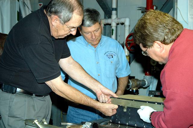 KENNEDY SPACE CENTER, FLA. -- United Space Alliance (USA) Vice President and Space Shuttle Program Manager Howard DeCastro (left) and NASA Deputy Associate Administrator for Space Station and Shuttle Programs Michael Kostelnik (center) are briefed on the use of a cold plate in Orbiter Processing Facility Bay 2 by a USA technician (right).  NASA and USA Space Shuttle program management are participating in a leadership workday.  The day is intended to provide management with an in-depth, hands-on look at Shuttle processing activities at KSC.