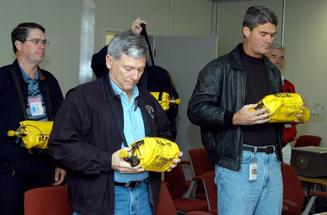 NASA image: KENNEDY SPACE CENTER, FLA. -- From front row left, NASA Deputy Associate Administrator for Space Station and Shuttle Programs Michael Kostelnik and NASA Space Shuttle Program Manager William Parsons are trained on the proper use of the Emergency Life Support Apparatus (ELSA).  NASA and United Space Alliance (USA) Space Shuttle program management are participating in a leadership workday.  The day is intended to provide management with an in-depth, hands-on look at Shuttle processing activities at KSC.