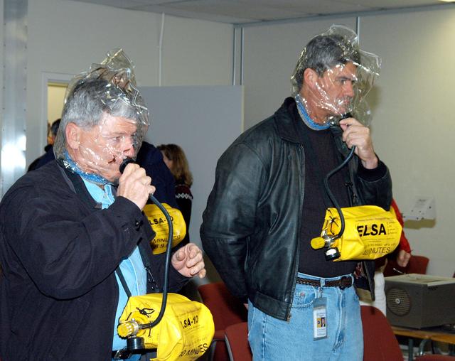 NASA image: KENNEDY SPACE CENTER, FLA. -- From left, NASA Deputy Associate Administrator for Space Station and Shuttle Programs Michael Kostelnik and NASA Space Shuttle Program Manager William Parsons each don an Emergency Life Support Apparatus (ELSA) during training on the proper use of the escape devices.  NASA and United Space Alliance (USA) Space Shuttle program management are participating in a leadership workday.  The day is intended to provide management with an in-depth, hands-on look at Shuttle processing activities at KSC.