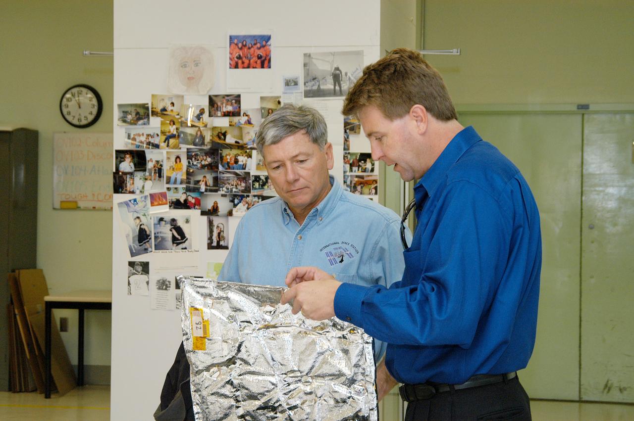 KENNEDY SPACE CENTER, FLA. -- United Space Alliance (USA) Manager of the Thermal Protection System (TPS) Facility Martin Wilson (right) briefs NASA Deputy Associate Administrator for Space Station and Shuttle Programs Michael Kostelnik (left) on the properties of a thermal blanket used in the Shuttle's TPS.  NASA and USA Space Shuttle program management are participating in a leadership workday.  The day is intended to provide management with an in-depth, hands-on look at Shuttle processing activities at KSC.