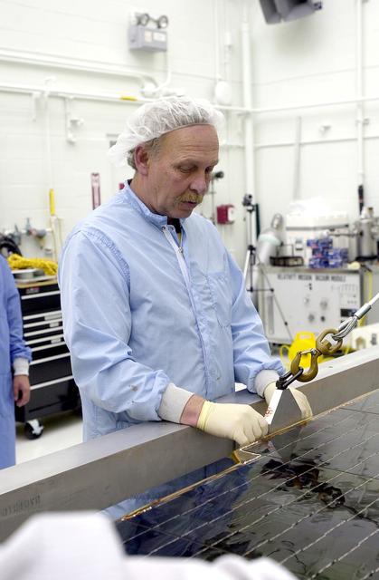 NASA image: VANDENBERG AFB, CALIF. - A worker in the NASA spacecraft processing facility on North Vandenberg Air Force Base adjust the supports on a solar array panel to be lifted and  installed on the Gravity Probe B spacecraft.  Installing each array is a 3-day process and includes a functional deployment test.  The Gravity Probe B mission is a relativity experiment developed by NASA’s Marshall Space Flight Center, Stanford University and Lockheed Martin.  The spacecraft will test two extraordinary predictions of Albert Einstein’s general theory of relativity that he advanced in 1916: the geodetic effect (how space and time are warped by the presence of the Earth) and frame dragging (how Earth’s rotation drags space and time around with it).  Gravity Probe B consists of four sophisticated gyroscopes that will provide an almost perfect space-time reference system.  The mission will look in a precision manner for tiny changes in the direction of spin.