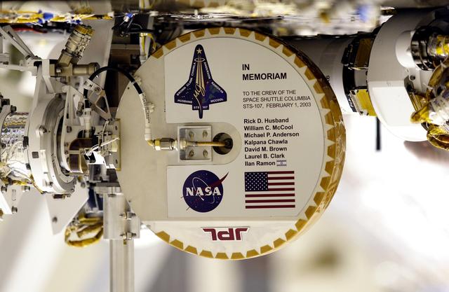 NASA image: KENNEDY SPACE CENTER, FLA. --Shown upside down to read the names, this plaque commemorating the STS-107 Space Shuttle Columbia crew now looks over the Mars landscape after the successful landing and deployment of the Mars Exploration Rover “Spirit” Jan. 4 onto the red planet.  The plaque, mounted on the high-gain antenna, is shown while the rover underwent final checkout March 28, 2003, in the Payload Hazardous Servicing Facility at KSC.