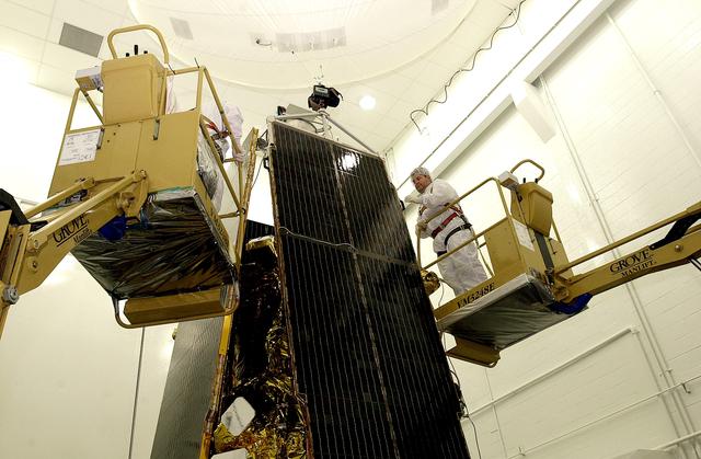 NASA image: VANDENBERG AFB, CALIF. -  In the NASA spacecraft processing facility on North Vandenberg Air Force Base, workers prepare to attach the top of a solar array panel onto the Gravity Probe B spacecraft.  Installing each array is a 3-day process and includes a functional deployment test.  The Gravity Probe B mission is a relativity experiment developed by NASA’s Marshall Space Flight Center, Stanford University and Lockheed Martin.  The spacecraft will test two extraordinary predictions of Albert Einstein’s general theory of relativity that he advanced in 1916: the geodetic effect (how space and time are warped by the presence of the Earth) and frame dragging (how Earth’s rotation drags space and time around with it).  Gravity Probe B consists of four sophisticated gyroscopes that will provide an almost perfect space-time reference system.  The mission will look in a precision manner for tiny changes in the direction of spin.