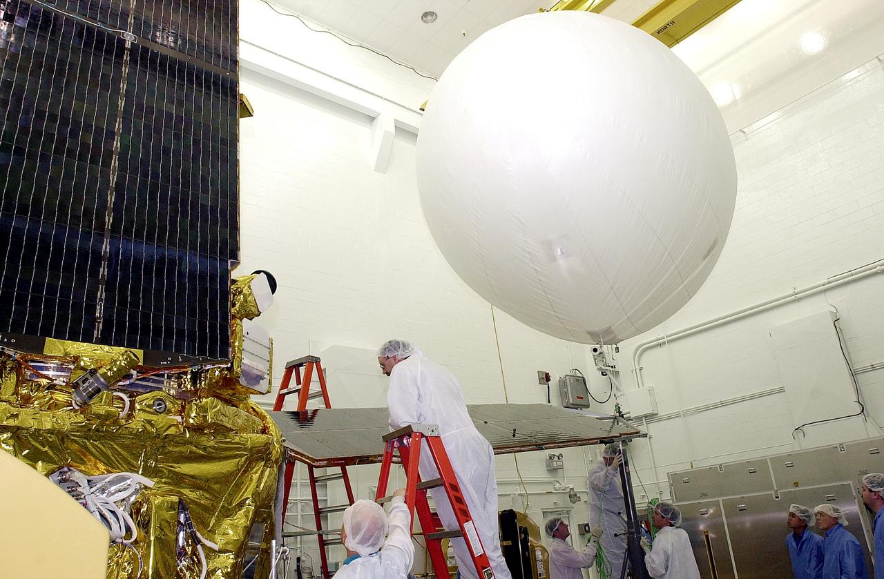 VANDENBERG AFB, CALIF. -  In the NASA spacecraft processing facility on North Vandenberg Air Force Base, workers stand by as the balloon at right is released to lift the solar array panel into position for installation on the Gravity Probe B spacecraft.  Installing each array is a 3-day process and includes a functional deployment test.  The Gravity Probe B mission is a relativity experiment developed by NASA’s Marshall Space Flight Center, Stanford University and Lockheed Martin.  The spacecraft will test two extraordinary predictions of Albert Einstein’s general theory of relativity that he advanced in 1916: the geodetic effect (how space and time are warped by the presence of the Earth) and frame dragging (how Earth’s rotation drags space and time around with it).  Gravity Probe B consists of four sophisticated gyroscopes that will provide an almost perfect space-time reference system.  The mission will look in a precision manner for tiny changes in the direction of spin.