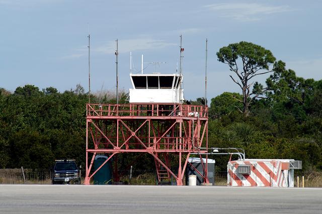 NASA image: KENNEDY SPACE CENTER, FLA. -- The existing control tower seen here at the edge of the KSC Shuttle Landing Facility is being replaced.  In use since 1987, the old tower stands only 20 feet above the runway surface, too low to see the launch pads to the east. During nighttime landing operations, those inside the tower have been hindered by the eight-billion candlepower xenon lights that illuminate the runway.  The new control tower is built atop an existing mound, rising nearly 100 feet over the midpoint of the runway.  The height gives controllers a spectacular 360-degree view of NASA-KSC and northern Brevard County. The new facility will also replace the SLF Operations Building. The operations building is home to the Military Radar Unit that monitors NASA-KSC airspace 24 hours a day, as well as runway light controls, navigational aids, weather and wind speed instrumentation, and gate controls. In the new tower, the computer displays will be fully modernized to Federal Aviation Administration standards with touch-screen technology. Construction on the new facility began in February 2003 and is nearly ready for occupancy. Only some final inspections and approvals remain. A support building and Public Affairs viewing deck, to be used for observing future landing operations, will be added and are already in work.