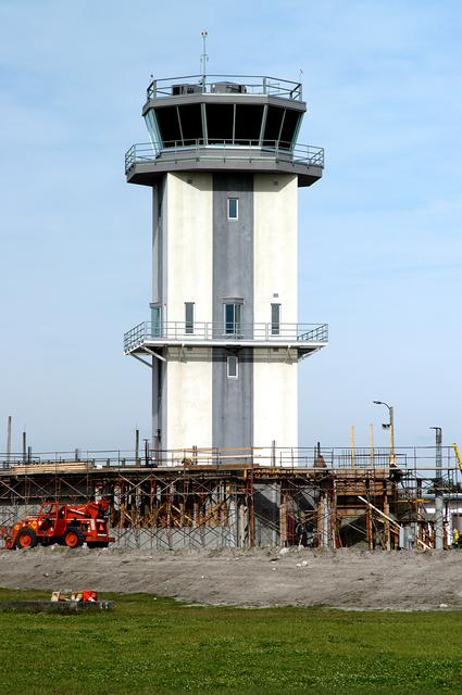 NASA image: KENNEDY SPACE CENTER, FLA. -- A new control tower is nearing completion at the KSC Shuttle Landing Facility.  It will replace the old tower in use since 1987.   The old tower stands only 20 feet above the runway surface, too low to see the launch pads to the east. During nighttime landing operations, those inside the tower have been hindered by the eight-billion candlepower xenon lights that illuminate the runway.  The new control tower is built atop an existing mound, rising nearly 100 feet over the midpoint of the runway.  The height gives controllers a spectacular 360-degree view of NASA-KSC and northern Brevard County. The new facility will also replace the SLF Operations Building. The operations building is home to the Military Radar Unit that monitors NASA-KSC airspace 24 hours a day, as well as runway light controls, navigational aids, weather and wind speed instrumentation, and gate controls. In the new tower, the computer displays will be fully modernized to Federal Aviation Administration standards with touch-screen technology. Construction on the new facility began in February 2003 and is nearly ready for occupancy. Only some final inspections and approvals remain. A support building and Public Affairs viewing deck, to be used for observing future landing operations, will be added and are already in work.
