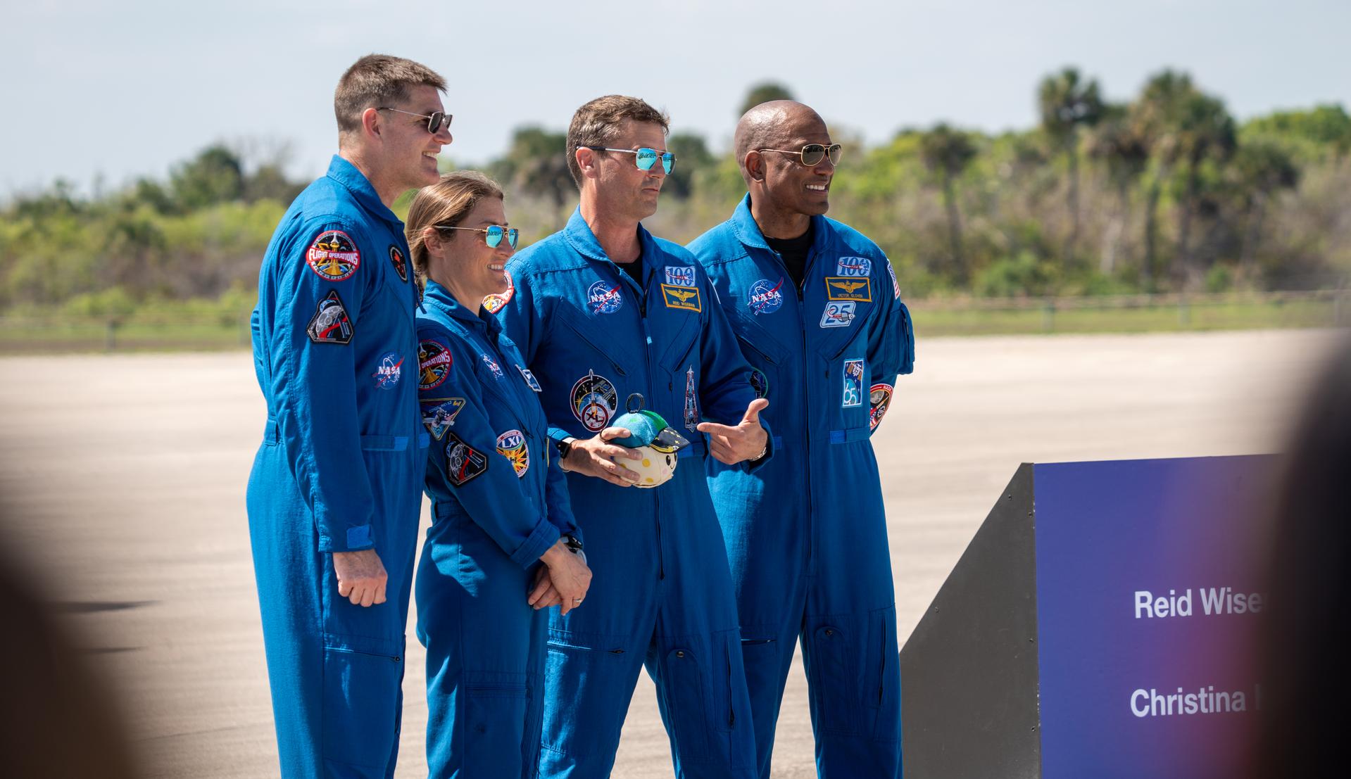 These images show the moments shortly after the arrival of the Artemis II crew to NASA’s Kennedy Space Center ahead of the launch. The four astronauts, Victor Glover, Reid Wiseman, Christina Koch, and Jeremy Hansen, are seen wearing their blue flight suits. They arrived on a white T38, which can be seen behind them with the NASA meatball on the side. They took turns speaking to the crowd as they also announced the zero-gravity indicator (ZGI) they would be taking with them on their journey. The ZGI is a little plush shaped like the Earth and is wearing a baseball hat.