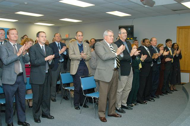 NASA image: KENNEDY SPACE CENTER, FLA. -- From the KSC television studio, KSC management and other employees applaud President George W. Bush, who addressed the public and an assembly of government officials at NASA Headquarters as he outlined a new focus and vision for the space agency.  Shown from left are Mike Leinbach, Shuttle launch director; David Culp, with NASA; Steve Francois, director, Launch Services Program; Richard Cota, deputy chief financial officer, KSC; Bill Pickavance vice president and associate program manager of Florida Operations, United Space Alliance (USA) ; Howard DeCastro, vice president and Space Shuttle program manager, USA; Shannon Roberts, with External Affairs; Woodrow Whitlow, KSC deputy director; Bruce Buckingham, assistant to Dr. Whitlow; Lisa Malone, director of External Affairs; Ken Aguilar, chief, Equal Opportunity office; and Cheryl Cox, External Affairs.  The President stated his goals for NASA’s new mission: Completing the International Space Station, retiring the Space Shuttle orbiters, developing a new crew exploration vehicle, and returning to the moon and beyond within the next two decades.   Pres. Bush was welcomed by NASA Administrator Sean O’Keefe and Expedition 8 Commander Michael Foale, who greeted him from the International Space Station.  Members of the Washington, D.C., audience included astronauts Eileen Collins, Ed Lu and Michael Lopez-Alegria, and former astronaut Gene Cernan