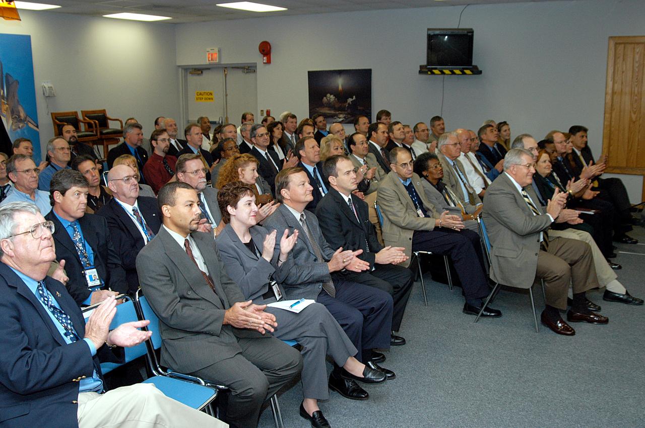 KENNEDY SPACE CENTER, FLA. -- From the KSC television studio, KSC management and other employees applaud President George W. Bush, who addressed the public and an assembly of government officials at NASA Headquarters, outlining a new focus and vision for the space agency.  Fourth from left is Mike Leinbach, Shuttle launch director; at right, front row, are Bill Pickavance vice president and associate program manager of Florida Operations, United Space Alliance (USA)  and Howard DeCastro, USA vice president and Space Shuttle program manager.  The President stated his goals for NASA’s new mission: Completing the International Space Station, retiring the Space Shuttle orbiters, developing a new crew exploration vehicle, and returning to the moon and beyond within the next two decades.   Pres. Bush was welcomed by NASA Administrator Sean O’Keefe and Expedition 8 Commander Michael Foale, who greeted him from the International Space Station.  Members of the Washington, D.C., audience included astronauts Eileen Collins, Ed Lu and Michael Lopez-Alegria, and former astronaut Gene Cernan.
