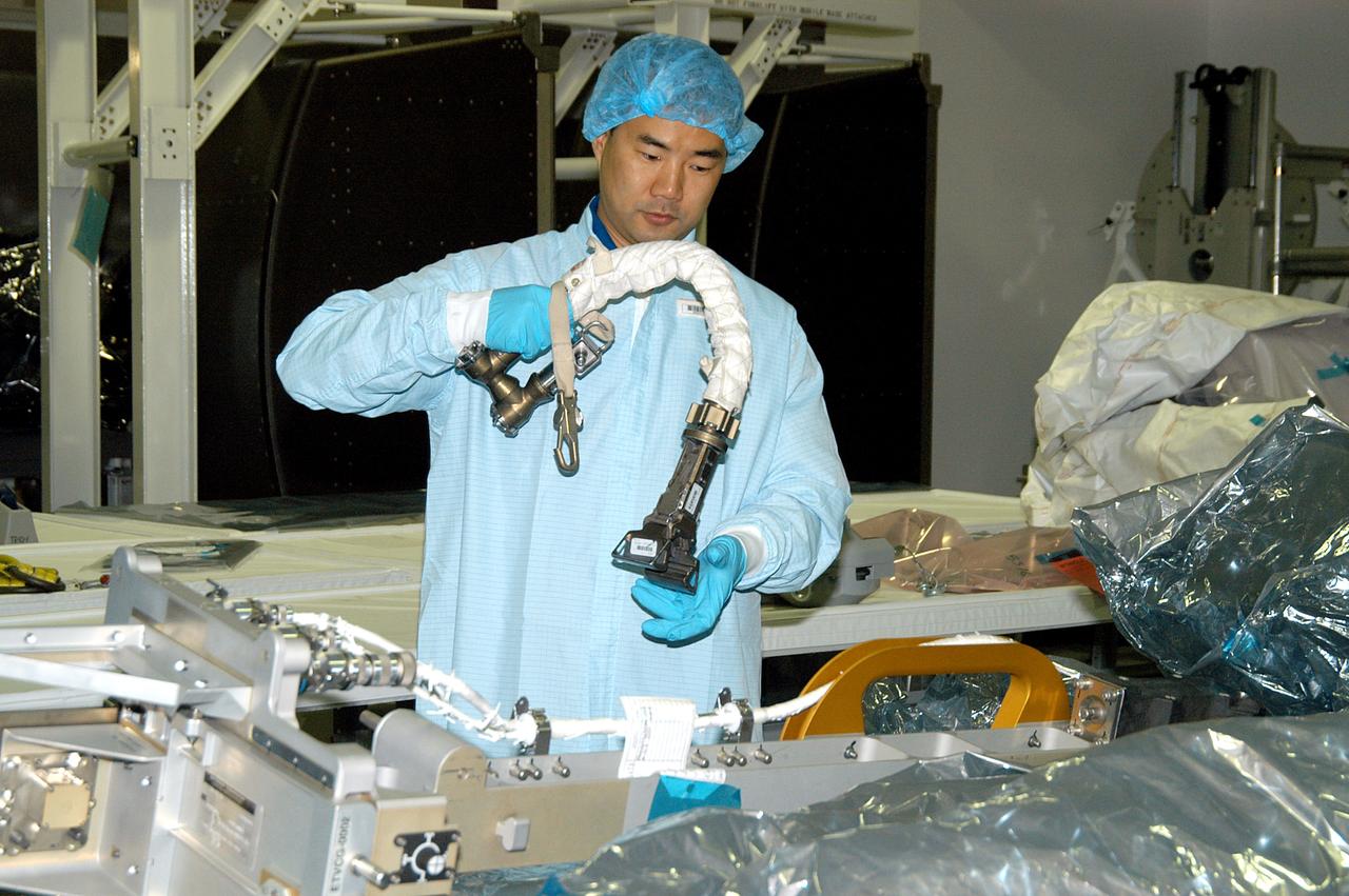 KENNEDY SPACE CENTER, FLA. -  Dressed in protective suits, STS-114 Mission Specialist Soichi Noguchi, with the Japanese Aerospace Exploration Agency (JAXA), handles equipment that will be used on the mission.  He and other crew members are at KSC for equipment familiarization.  STS-114 is classified as Logistics Flight 1 to the International Space Station, delivering new supplies and replacing one of the orbital outpost’s Control Moment Gyroscopes (CMGs). STS-114 will also carry a Raffaello Multi-Purpose Logistics Module and the External Stowage Platform-2.  The crew is slated to conduct at least three spacewalks: They will demonstrate repair techniques of the Shuttle’s Thermal Protection System,  replace the failed CMG with one delivered by the Shuttle, and  install the External Stowage Platform.