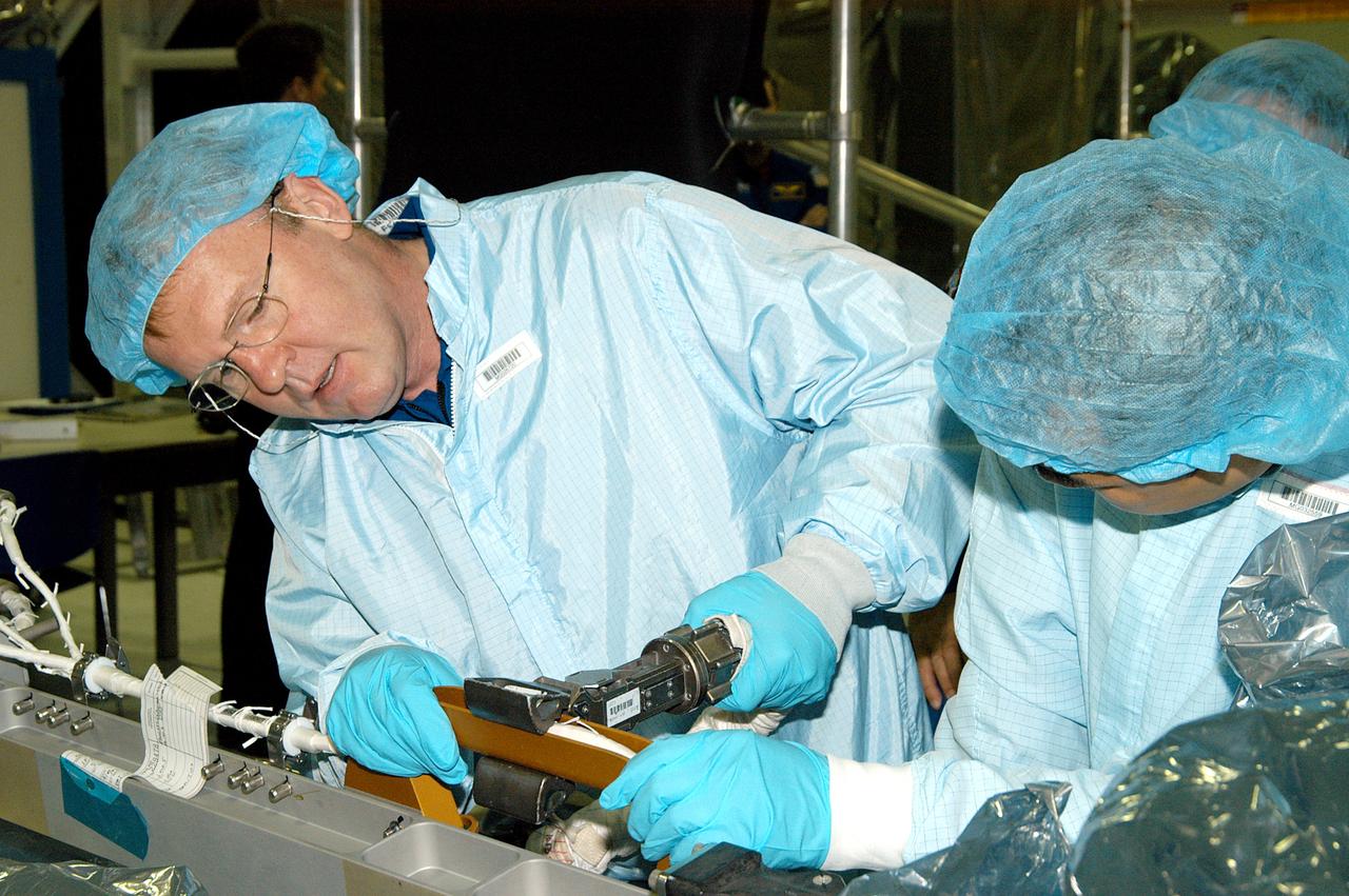 KENNEDY SPACE CENTER, FLA. -  In the Space Station Processing Facility, STS-114 Mission Specialist Andrew Thomas (left) works with equipment while Mission Specialist Soichi Noguchi watches.  Noguchi is with the Japanese Aerospace Exploration Agency (JAXA).  They and other crew members are at KSC for equipment familiarization.  STS-114 is classified as Logistics Flight 1 to the International Space Station, delivering new supplies and replacing one of the orbital outpost’s Control Moment Gyroscopes (CMGs). STS-114 will also carry a Raffaello Multi-Purpose Logistics Module and the External Stowage Platform-2.  The crew is slated to conduct at least three spacewalks: They will demonstrate repair techniques of the Shuttle’s Thermal Protection System,  replace the failed CMG with one delivered by the Shuttle, and  install the External Stowage Platform.