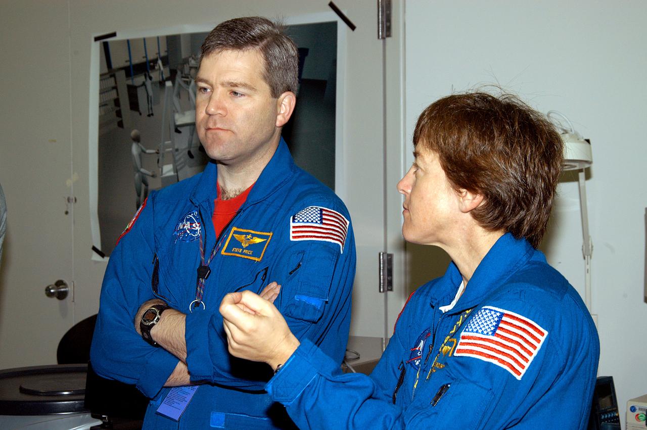 KENNEDY SPACE CENTER, FLA. -  In the Space Station Processing Facility, astronaut Stephen Frick and STS-114 Mission Specialist Wendy Lawrence watch as crew members work with equipment that will be used on the mission.  Frick is a tile specialist, who joined the STS-114 crew during equipment familiarization at KSC. STS-114 is classified as Logistics Flight 1 to the International Space Station, delivering new supplies and replacing one of the orbital outpost’s Control Moment Gyroscopes (CMGs). STS-114 will also carry a Raffaello Multi-Purpose Logistics Module and the External Stowage Platform-2.  The crew is slated to conduct at least three spacewalks: They will demonstrate repair techniques of the Shuttle’s Thermal Protection System,  replace the failed CMG with one delivered by the Shuttle, and  install the External Stowage Platform.