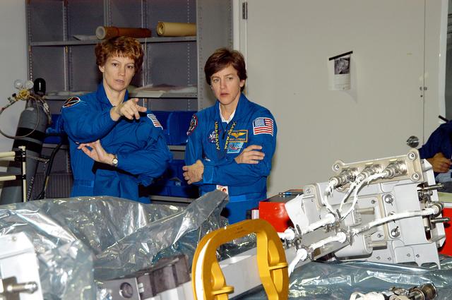 NASA image: KENNEDY SPACE CENTER, FLA. -  STS-114 Commander Eileen Collins and Mission Specialist Wendy Lawrence look over mission equipment in the Space Station Processing Facility.  Crew members are at KSC for equipment familiarization.  STS-114 is classified as Logistics Flight 1 to the International Space Station, delivering new supplies and replacing one of the orbital outpost’s Control Moment Gyroscopes (CMGs). STS-114 will also carry a Raffaello Multi-Purpose Logistics Module and the External Stowage Platform-2.  The crew is slated to conduct at least three spacewalks: They will demonstrate repair techniques of the Shuttle’s Thermal Protection System,  replace the failed CMG with one delivered by the Shuttle, and  install the External Stowage Platform.
