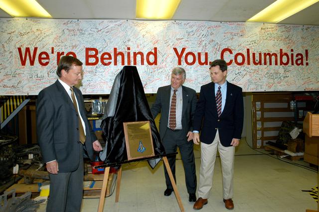 NASA image: KENNEDY SPACE CENTER, FLA. -  In the Vehicle Assembly Building, Shuttle Launch Director Mike Leinbach, Center Director Jim Kennedy and NASA Vehicle Manager Scott Thurston unveil a plaque honoring “Columbia, the crew of STS-107, and their loved ones.”  The site is the “Columbia room,” a permanent repository of the debris collected in the aftermath of the tragic accident Feb. 1, 2003, that claimed the orbiter and lives of the seven-member crew.  The dedication of the plaque was made in front of the 40-member preservation team.