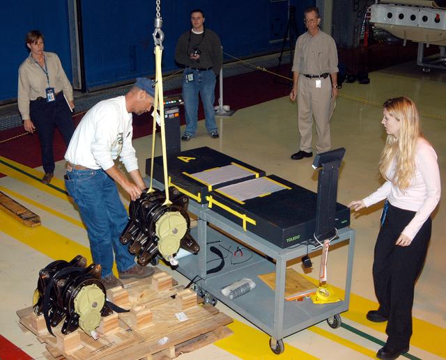 NASA image: KENNEDY SPACE CENTER, FLA. -  Workers in the Orbiter Processing Facility stand by while another guides the lifting of one of two rudder speed brake actuators onto a table to measure the alignment of its bearings.  The actuators move an orbiter’s rudder, speed brake, elevons and main engines during flight.