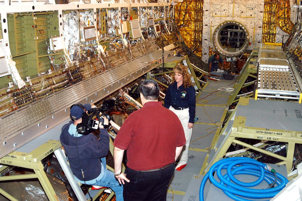KENNEDY SPACE CENTER, FLA. -  Standing inside Discovery’s payload bay, Carol Scott (right), lead orbiter engineer, talks about her job as part of a special feature for the KSC Web.  With his back to the camera is Bill Kallus, Media manager in the KSC Web Studio.  Behind Scott can be seen the open hatch of the airlock, which provides support functions such as airlock depressurization and repressurization, extravehicular activity equipment recharge, liquid-cooled garment water cooling, EVA equipment checkout, donning and communications. The outer hatch isolates the airlock from the unpressurized payload bay when closed and permits the EVA crew members to exit from the airlock to the payload bay when open.