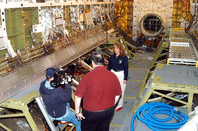 NASA image: KENNEDY SPACE CENTER, FLA. -  Standing inside Discovery’s payload bay, Carol Scott (right), lead orbiter engineer, talks about her job as part of a special feature for the KSC Web.  With his back to the camera is Bill Kallus, Media manager in the KSC Web Studio.  Behind Scott can be seen the open hatch of the airlock, which provides support functions such as airlock depressurization and repressurization, extravehicular activity equipment recharge, liquid-cooled garment water cooling, EVA equipment checkout, donning and communications. The outer hatch isolates the airlock from the unpressurized payload bay when closed and permits the EVA crew members to exit from the airlock to the payload bay when open.