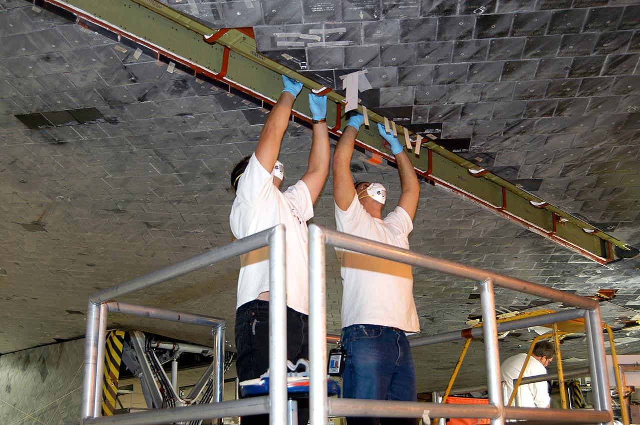 KENNEDY SPACE CENTER, FLA. -  In the Orbiter Processing Facility, technicians work on insulation tiles near the landing gear door of orbiter Discovery.  The orbiter is now being prepared for eventual launch on a future mission.