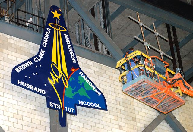 KENNEDY SPACE CENTER, FLA. -  Workers install a 20-foot by 15-foot replica of the STS-107 logo above the “A” on the A tower in the transfer aisle of the Vehicle Assembly Building.  The debris from the orbiter Columbia, lost in a tragic accident on its return to Earth from the STS-107 mission, is permanently stored in the tower.  A dedication ceremony Jan. 29, 2004, revealed a plaque being installed in the storage area in honor of “Columbia, the crew of STS-107, and their loved ones.”