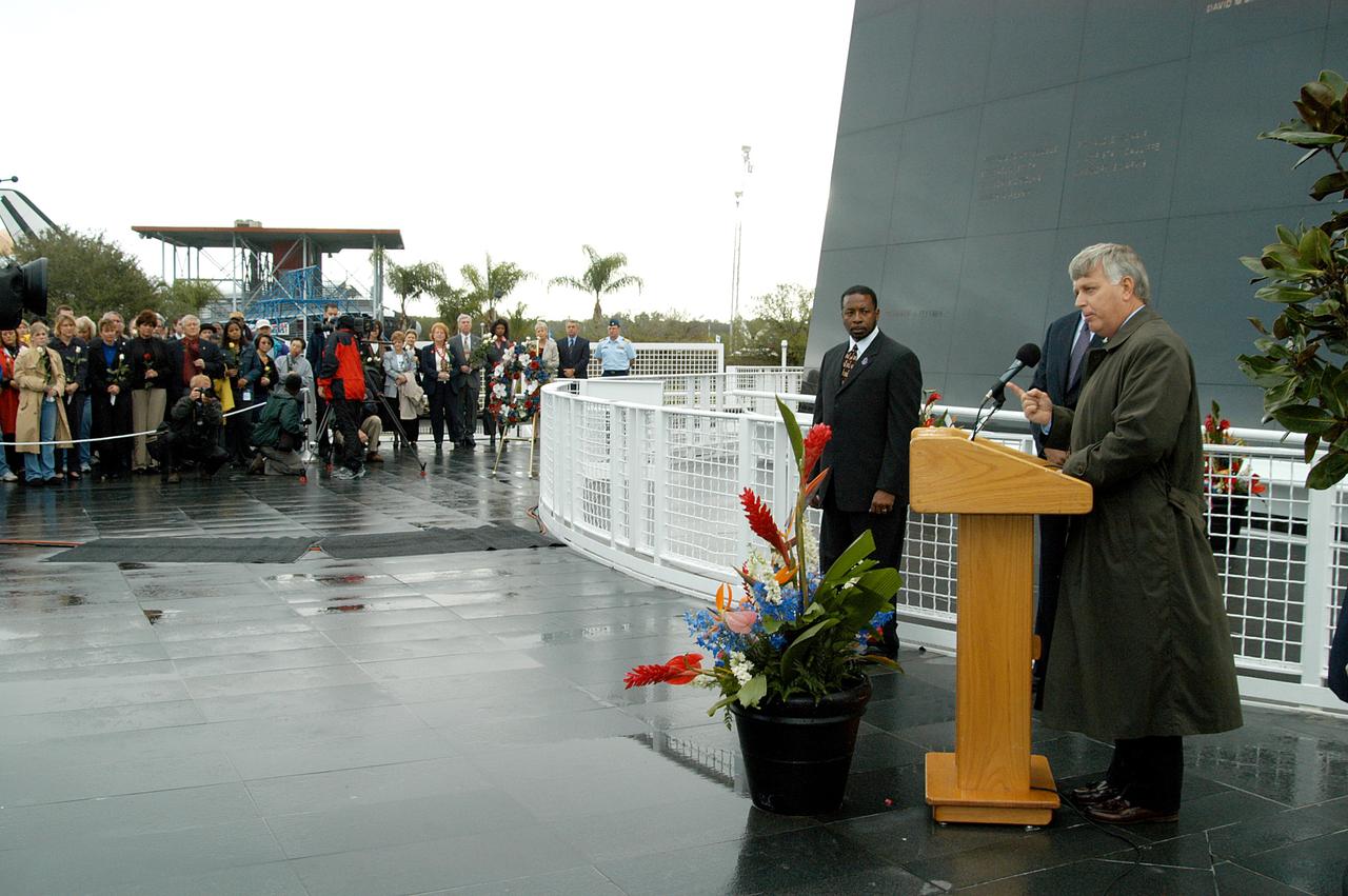 KENNEDY SPACE CENTER, FLA. -  Center Director Jim Kennedy (right) speaks to attendees at a memorial service honoring the crew of Columbia.  Behind him are KSC Deputy Director Woodrow Whitlow Jr. and Executive Director of Florida Space Authority Winston Scott, who is a former astronaut who flew on Columbia in 1997. They are standing in front of the Space Memorial Mirror at the KSC Visitor Complex.  Attended by many friends, co-workers and families, the memorial service was also open to the public, some of whom are seen at left.  Feb. 1 is the one-year anniversary of the loss of the crew and orbiter Columbia in a tragic accident as the ship returned to Earth following mission STS-107.