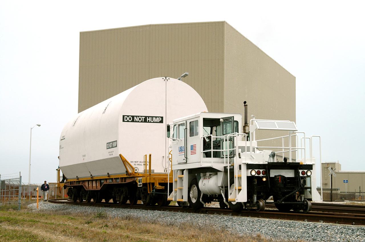 KENNEDY SPACE CENTER, FLA. - An engine pulls the container enclosing a segment of a solid rocket booster from the Rotation Processing and Surge Facility.  The container will join others on the main track for a trip to Utah where the segments will undergo firing.  The segments were part of the STS-114 stack.  It is the first time actual flight segments that had been stacked for flight in the VAB are being returned for testing.  They will undergo firing, which will enable inspectors to check the viability of the solid and verify the life expectancy for stacked segments.