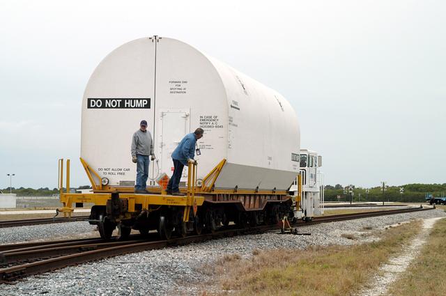 NASA image: KENNEDY SPACE CENTER, FLA. - Workers ride the rails along with a container enclosing a segment of a solid rocket booster being moved to the main track.  Several segments are being returned to Utah for testing.  The segments were part of the STS-114 stack.  It is the first time actual flight segments that had been stacked for flight in the VAB are being returned for testing.  They will undergo firing, which will enable inspectors to check the viability of the solid and verify the life expectancy for stacked segments.