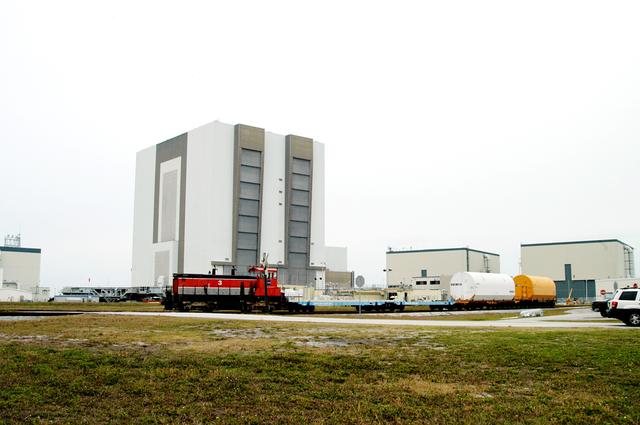 NASA image: KENNEDY SPACE CENTER, FLA. - Moving past the 525-foot-high Vehicle Assembly Building, the red NASA engine pulls several containers enclosing segments of a solid rocket booster being returned to Utah for testing.  The segments were part of the STS-114 stack.  It is the first time actual flight segments that had been stacked for flight in the VAB are being returned for testing.  They will undergo firing, which will enable inspectors to check the viability of the solid and verify the life expectancy for stacked segments.