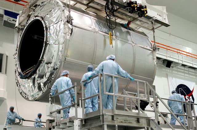 NASA image: KENNEDY SPACE CENTER, FLA. - Workers watch as the Multi-Purpose Logistics Module Raffaello is lowered toward a work stand in the Space Station Processing Facility.  Raffaello is the second MPLM built by the Italian Space Agency, serving as a reusable logistics carrier and primary delivery system to resupply and return station cargo requiring a pressurized environment.  It has been moved across the floor to allow the third MPLM, Donatello, to be brought in for routine testing.  Donatello has been stored in the Operations and Checkout Building.  This is the first time all three MPLMs are in the SSPF; the other one is the Leonardo.  Raffaello is scheduled to fly on Space Shuttle Atlantis on mission STS-114.