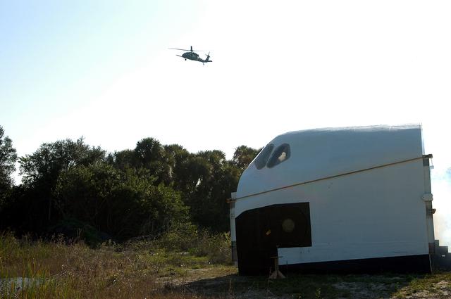 NASA image: KENNEDY SPACE CENTER, FLA. - A helicopter approaches an orbiter crew compartment mock-up as part of a “Mode VII” emergency landing simulation at Kennedy Space Center.  The purpose is to exercise emergency preparedness personnel, equipment and facilities in rescuing astronauts from a downed orbiter and providing immediate medical attention.  This simulation presents an orbiter that has crashed short of the Shuttle Landing Facility in a wooded area 2-1/2 miles south of Runway 33.  Emergency crews will respond to the volunteer “astronauts” simulating various injuries.  Rescuers must remove the crew, provide triage and transport to hospitals those who need further treatment.  Local hospitals are participating in the exercise.