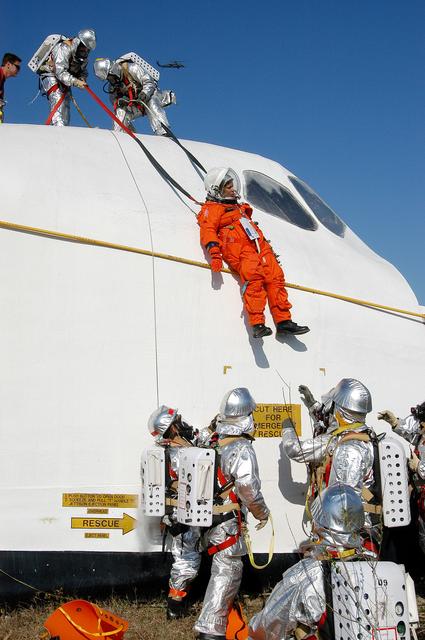 NASA image: KENNEDY SPACE CENTER, FLA. - Emergency crew members lower a volunteer “astronaut” from the top of the orbiter crew compartment mock-up that is the scene of a “Mode VII” emergency landing simulation at Kennedy Space Center.  The purpose of the Mode VII is to exercise emergency preparedness personnel, equipment and facilities in rescuing astronauts from a downed orbiter and providing immediate medical attention.  This simulation presents an orbiter that has crashed short of the Shuttle Landing Facility in a wooded area 2-1/2 miles south of Runway 33.  Emergency crews are responding to the volunteer “astronauts” who are simulating various injuries.  Rescuers must remove the crew, provide triage and transport to hospitals those who need further treatment.  Local hospitals are participating in the exercise.