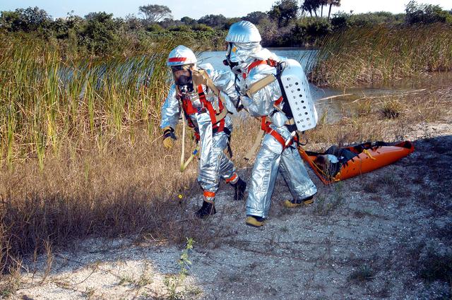 NASA image: KENNEDY SPACE CENTER, FLA. - Emergency crew members transport an “injured” astronaut during a “Mode VII” emergency landing simulation at Kennedy Space Center.  The purpose of the Mode VII is to exercise emergency preparedness personnel, equipment and facilities in rescuing astronauts from a downed orbiter and providing immediate medical attention.  This simulation presents an orbiter that has crashed short of the Shuttle Landing Facility in a wooded area 2-1/2 miles south of Runway 33.  Emergency crews are responding to the volunteer astronauts who are simulating various injuries.  Rescuers must remove the crew, provide triage and transport to hospitals those who need further treatment.  Local hospitals are participating in the exercise.