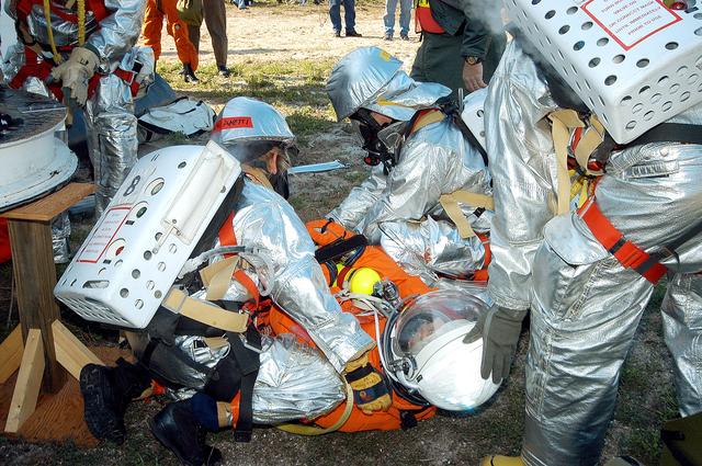 NASA image: KENNEDY SPACE CENTER, FLA. - Emergency crew members help an injured astronaut after removing him from the orbiter crew compartment mock-up during a “Mode VII” emergency landing simulation at Kennedy Space Center.  The purpose of the Mode VII is to exercise emergency preparedness personnel, equipment and facilities in rescuing astronauts from a downed orbiter and providing immediate medical attention.  This simulation presents an orbiter that has crashed short of the Shuttle Landing Facility in a wooded area 2-1/2 miles south of Runway 33.  Emergency crews are responding to the volunteer astronauts who are simulating various injuries.  Rescuers must remove the crew, provide triage and transport to hospitals those who need further treatment.  Local hospitals are participating in the exercise.