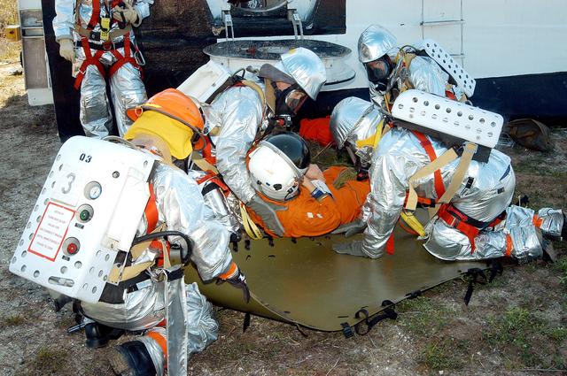 NASA image: KENNEDY SPACE CENTER, FLA. - Emergency crew members help an “injured” astronaut who was removed from the orbiter crew compartment mock-up during a “Mode VII” emergency landing simulation at Kennedy Space Center.  The purpose of the Mode VII is to exercise emergency preparedness personnel, equipment and facilities in rescuing astronauts from a downed orbiter and providing immediate medical attention.  This simulation presents an orbiter that has crashed short of the Shuttle Landing Facility in a wooded area 2-1/2 miles south of Runway 33.  Emergency crews are responding to the volunteer astronauts who are simulating various injuries.  Rescuers must remove the crew, provide triage and transport to hospitals those who need further treatment.  Local hospitals are participating in the exercise.