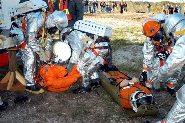 NASA image: KENNEDY SPACE CENTER, FLA. - Emergency crew members assess medical needs on “injured” astronauts removed from the orbiter crew compartment mock-up during a “Mode VII” emergency landing simulation at Kennedy Space Center.  The purpose of the Mode VII is to exercise emergency preparedness personnel, equipment and facilities in rescuing astronauts from a downed orbiter and providing immediate medical attention.  This simulation presents an orbiter that has crashed short of the Shuttle Landing Facility in a wooded area 2-1/2 miles south of Runway 33.  Emergency crews are responding to the volunteer astronauts who are simulating various injuries.  Rescuers must remove the crew, provide triage and transport to hospitals those who need further treatment.  Local hospitals are participating in the exercise.