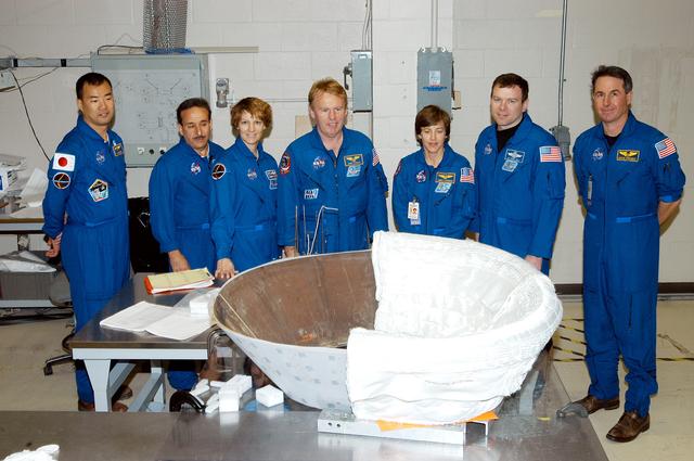 NASA image: KENNEDY SPACE CENTER, FLA. - The STS-114 crew gathers around the work stand holding the insert for Discovery’s nose cap.  From left are Mission Specialists Soichi Noguchi, and Charles Camarda; Commander Eileen Collins; Mission Specialists Andrew Thomas and Wendy Lawrence; Pilot James Kelly; and Mission Specialist Stephen Robinson. Noguchi represents the Japanese Aerospace and Exploration Agency.  The insert is being fitted with thermal protection system insulation blankets.  The crew is spending time becoming familiar with Shuttle and mission equipment.  The mission is Logistics Flight 1, which is scheduled to deliver supplies and equipment plus the external stowage platform to the International Space Station.