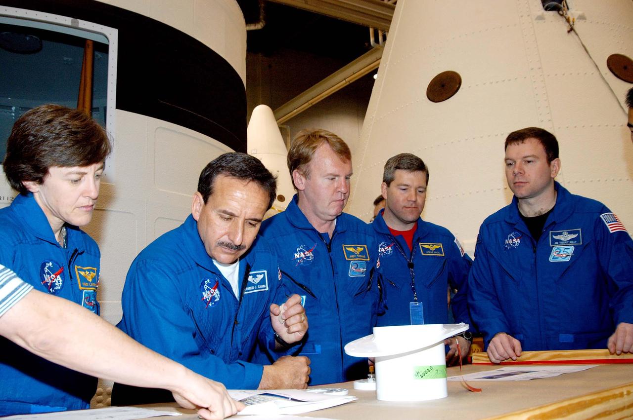 KENNEDY SPACE CENTER, FLA. -  Framed by segments of solid rocket boosters in the SRB Assembly and Refurbishment Facility, STS-114 crew members look at external tank-solid rocket booster camera components.  From left are Mission Specialists Wendy Lawrence, Charles Camarda and Andrew Thomas; astronaut Steven Frick; and Pilot James Kelly. Frick joined the STS-114 crew during equipment familiarization at KSC.  The STS-114 mission is Logistics Flight 1, which is scheduled to deliver supplies and equipment, plus the external stowage platform, to the International Space Station.