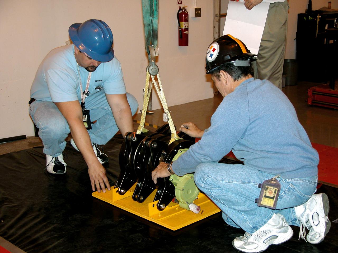 KENNEDY SPACE CENTER, FLA. -  Workers at Cape Canaveral Air Force Station place one of four rudder speed brake actuators onto a pallet for X-ray.  The actuators, to be installed on the orbiter Discovery, are being X-rayed at the Radiographic High-Energy X-ray Facility to determine if the gears were installed correctly. Discovery has been assigned to the first Return to Flight mission, STS-114, a logistics flight to the International Space Station.
