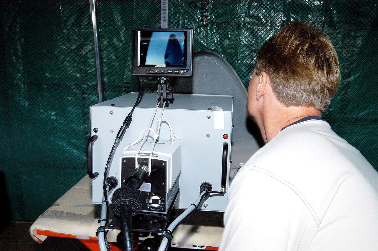 KENNEDY SPACE CENTER, FLA. -  Jim Landy, NDE specialist with United Space Alliance (USA), prepares equipment to examine a Reinforced Carbon Carbon panel using flash thermography.  A relatively new procedure at KSC, thermography uses high intensity light to heat areas of the panels. The panels are then immediately scanned with an infrared camera. As the panels cool, any internal flaws are revealed. The gray carbon composite RCC panels are attached to the leading edge of the wing of the orbiters.  They have sufficient strength to withstand the aerodynamic forces experienced during launch and reentry, which can reach as high as 800 pounds per square foot.  The operating range of RCC is from minus 250º F to about 3,000º F, the temperature produced by friction with the atmosphere during reentry. The panels will be installed on the orbiter Discovery, designated for the first Return to Flight mission, STS-114.