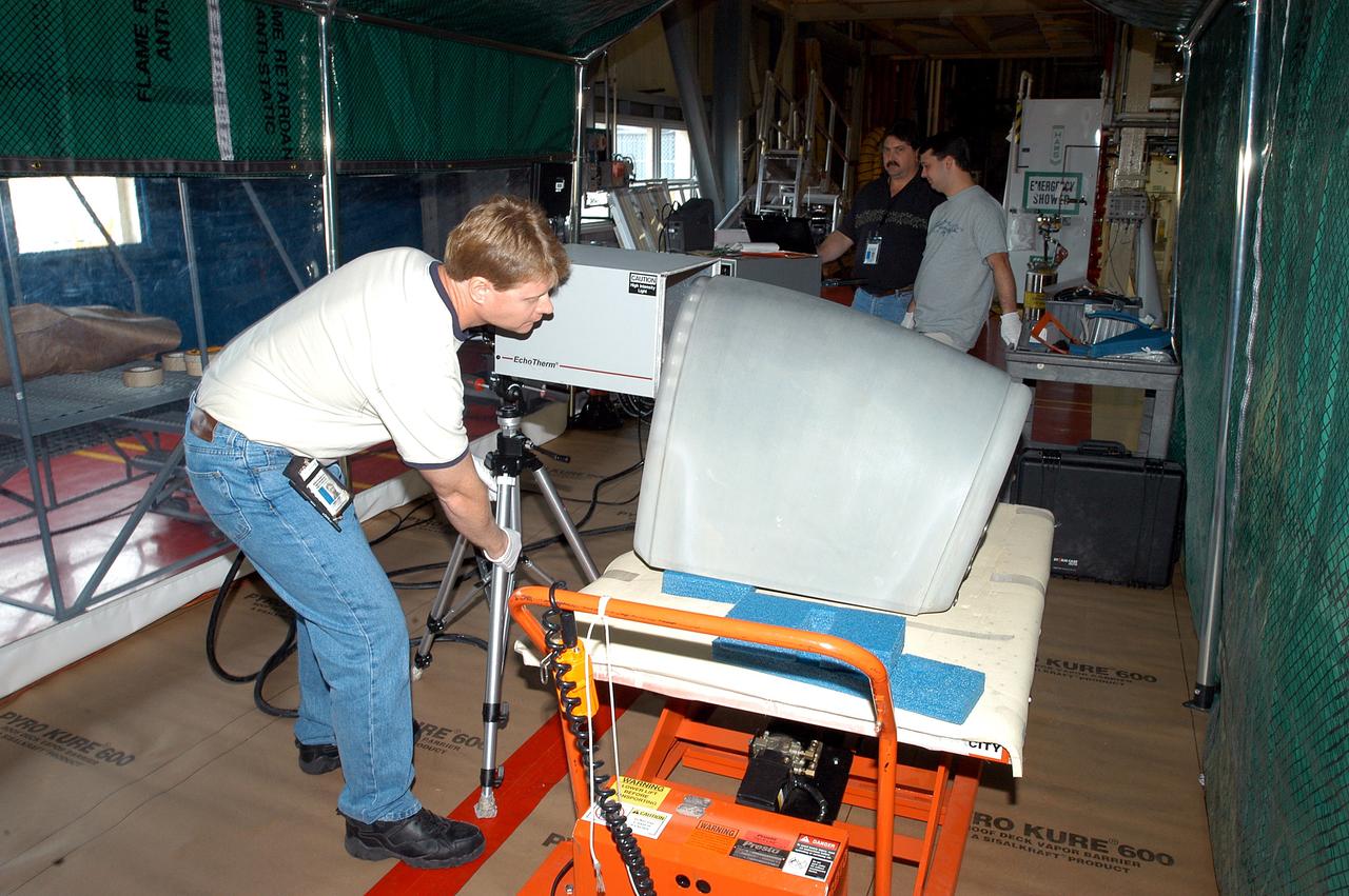 KENNEDY SPACE CENTER, FLA. -  Jim Landy, NDE specialist with United Space Alliance, sets up equipment to examine a Reinforced Carbon Carbon panel using flash thermography.  A relatively new procedure at KSC, thermography uses high intensity light to heat areas of the panels. The panels are then immediately scanned with an infrared camera. As the panels cool, any internal flaws are revealed. The gray carbon composite RCC panels are attached to the leading edge of the wing of the orbiters.  They have sufficient strength to withstand the aerodynamic forces experienced during launch and reentry, which can reach as high as 800 pounds per square foot.  The operating range of RCC is from minus 250º F to about 3,000º F, the temperature produced by friction with the atmosphere during reentry.  The panels will be installed on the orbiter Discovery, designated  for the first Return to Flight mission, STS-114.