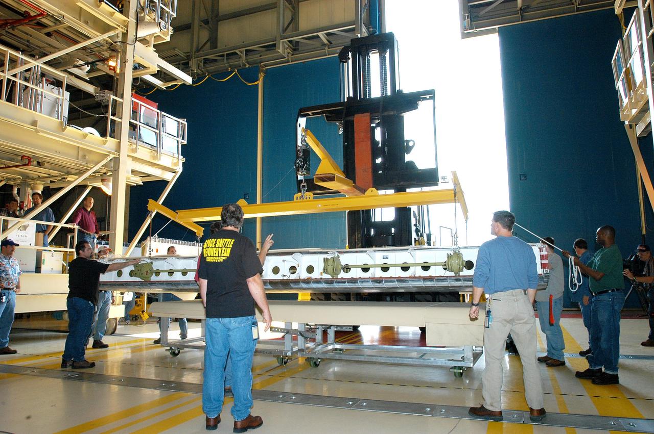 KENNEDY SPACE CENTER, FLA. -  Workers in the Orbiter Processing Facility help prepare the body flap for lifting prior to installation on the orbiter Discovery. The body flap is an aluminum structure consisting of ribs, spars, skin panels and a trailing edge assembly. It thermally shields the three main engines during entry and provides pitch control trim during landing approach.  Discovery is being processed for launch on the first Return to Flight mission, STS-114.