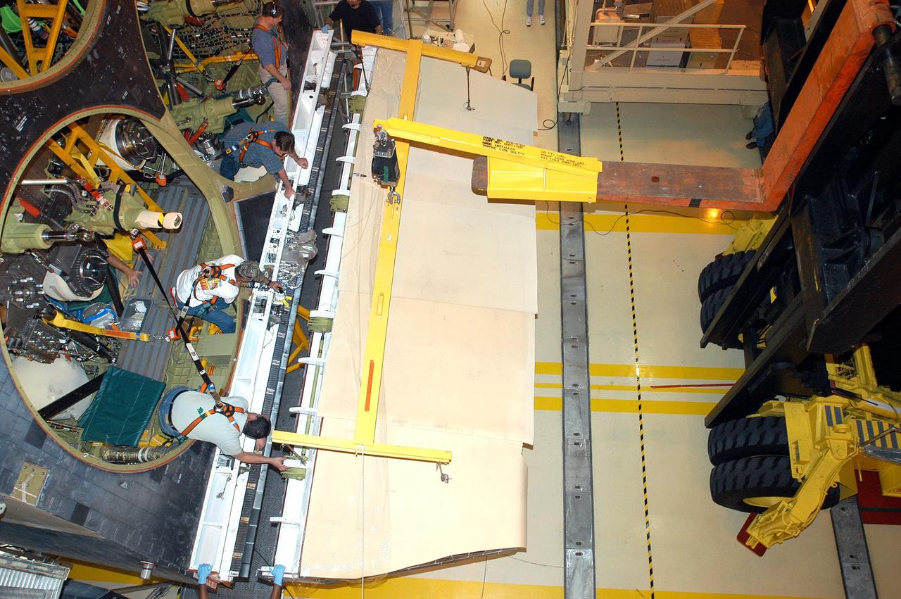 KENNEDY SPACE CENTER, FLA. -  Workers in the Orbiter Processing Facility lean toward the body flap to be installed on the orbiter Discovery.  The body flap is an aluminum structure consisting of ribs, spars, skin panels and a trailing edge assembly. It thermally shields the three main engines during entry and provides pitch control trim during landing approach.  Discovery is being processed for launch on the first Return to Flight mission, STS-114.